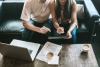 A couple on the couch reviewing their finances on the laptop and papers